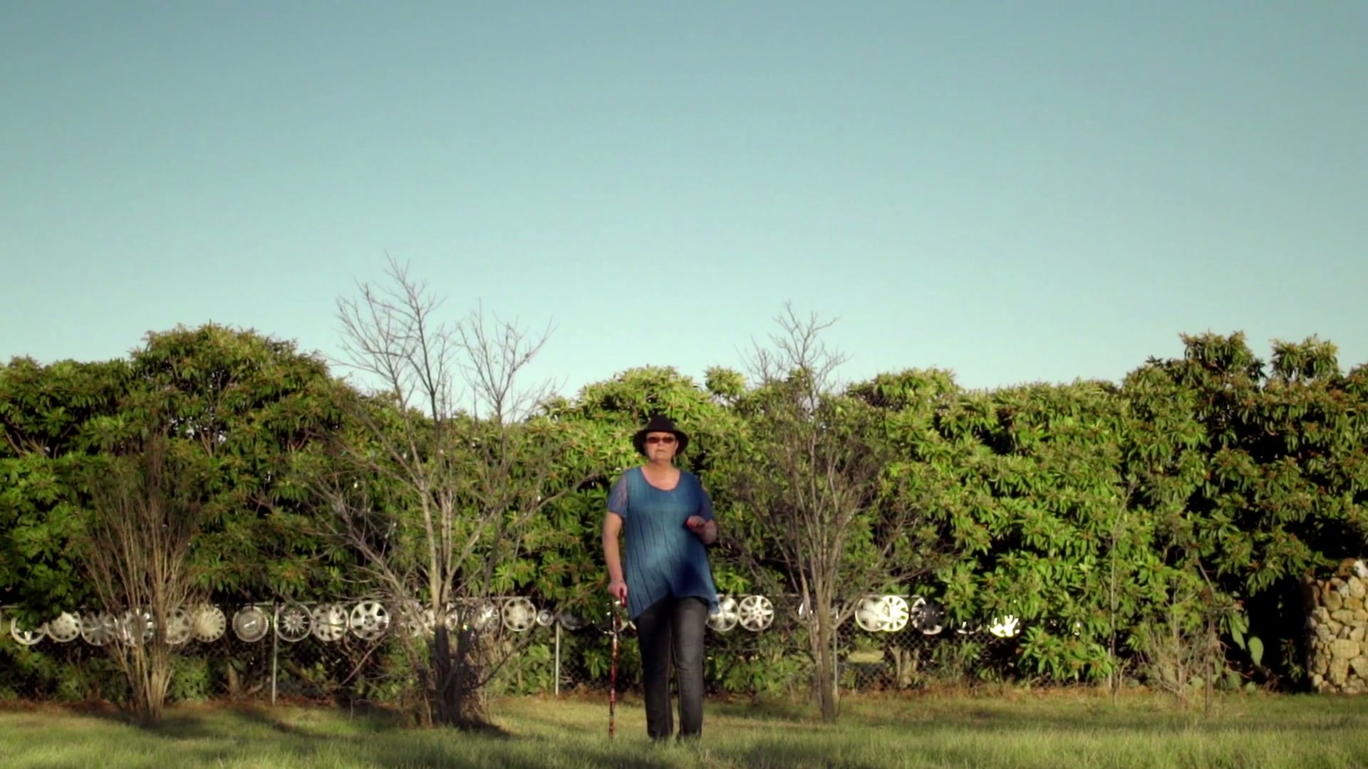 Erin stands in a grassy yard against a line of trees, with the open sky above her.