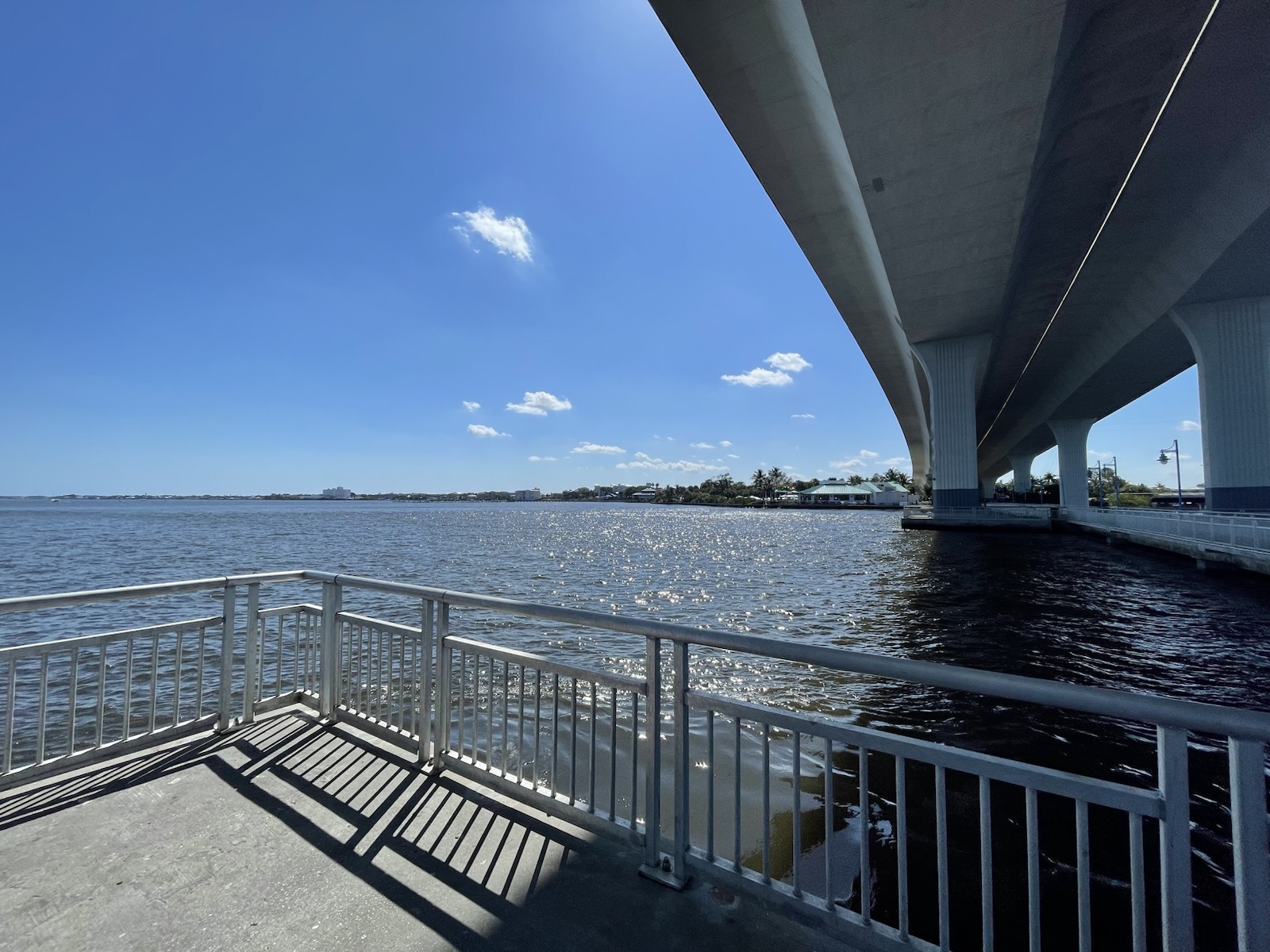 Modern bridge spanning open water above a waterfront walkway and railing.